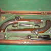 A Superb Cased Pair of Irish Percussion Travelling Pistols by Trulock & Son.Dublin. Circa 1835. 11 inches Overall with 6.1/4 inch Octagonal Twist, Rifled and Sighted Barrels. 'Dublin' to Top Flat. Owners name to Bottom Flat. 'Augustus H. Barton' He resided Rochetown Co Tipperary. 1814-1874. Back Action Locks. With Typical Wide Necked Hammers. Triple Bented Locks. Locks Engraved 'Trulock & Son.' ( 1822-1842). Captive Ramrods. Contained in Green Baize Lined Mahogany Case with Brass Hinges and Key Escutcheon. Lock with Key. Accoutrements include; Steel Bodied Pistol Flask with Brass Top & Charger. Ebony Loading / Cleaning Rod. Horn Handled Turnscrew. Nipple Key. Eley Percussion Cap Tin. Steel 24 Bore Pincer Bullet Mould.
